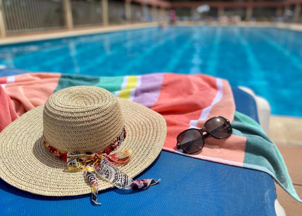 ALMA BEACH ESTARTIT في لو ايسترتيت: قبعة من القش ونظارة شمسية جالسة على كرسي بجوار حمام سباحة