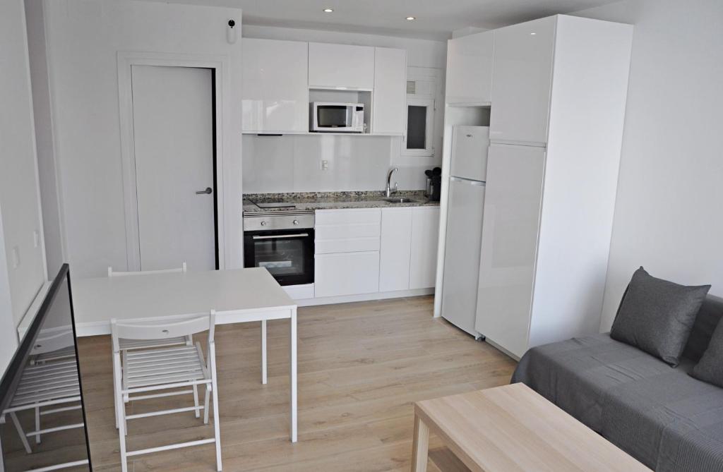 a white kitchen and living room with a table and a couch at Centro Sitges in Sitges