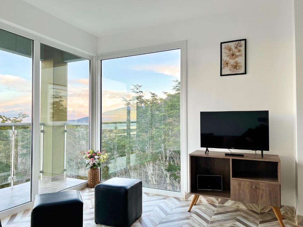 sala de estar con TV de pantalla plana y ventanas grandes. en Disfruta la vista del Canal de Beagle! Departamento tranquilo rodeado de Árboles y montañas en Ushuaia