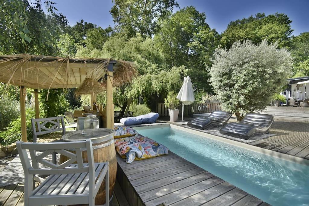 een zwembad met een terras en stoelen naast bij La villa du Petit Bois in Lignan-de-Bordeaux