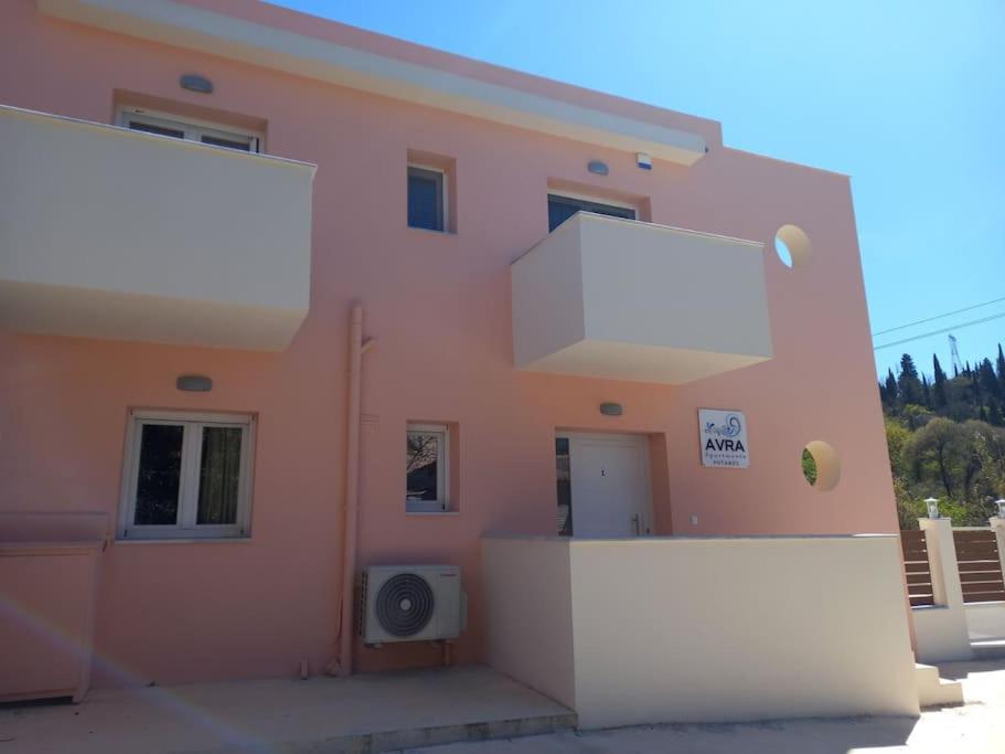 um edifício rosa com uma parede branca ao lado em AVRA-2 Apartments Potamos CORFU em Potamós