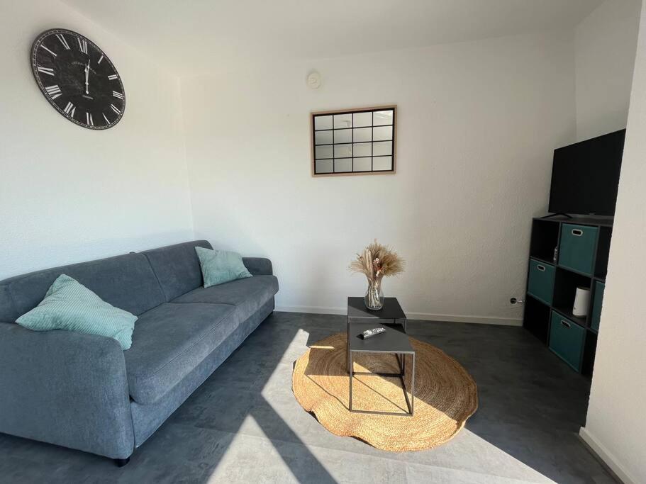 a living room with a blue couch and a clock at Studio 4 pers proche de la mer in Camiers