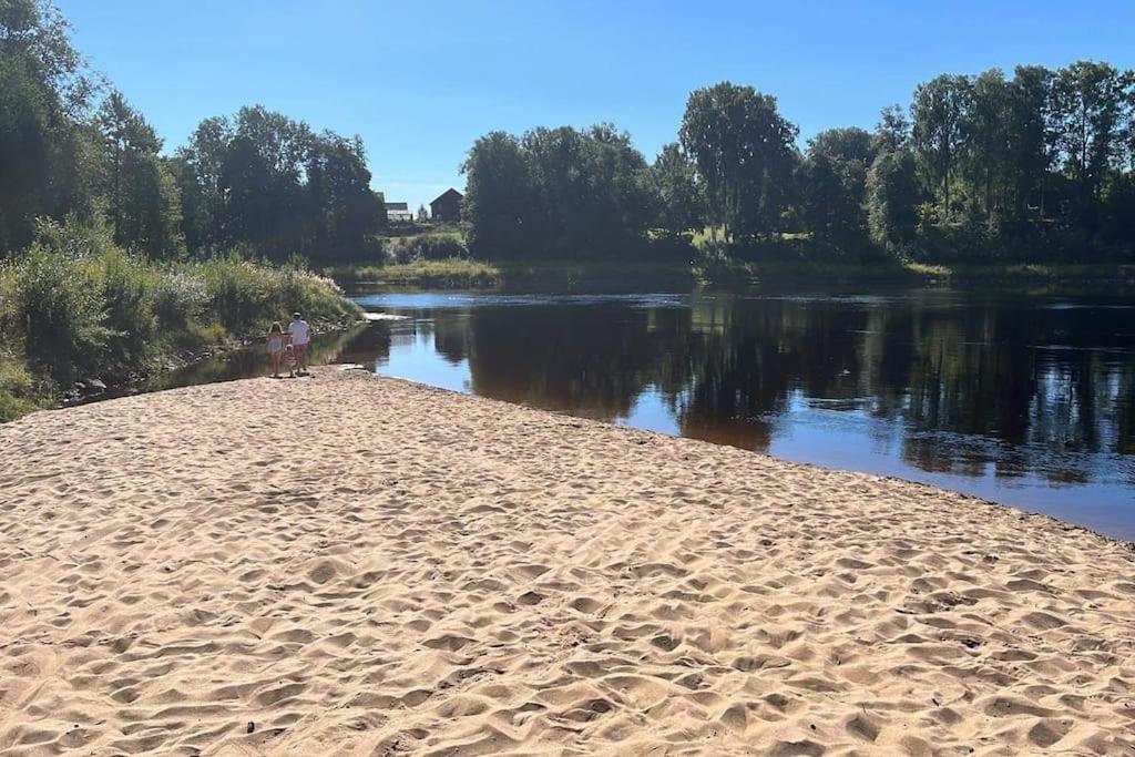 two people standing on a sandy beach next to a river at House by the Klaraelven in Forshaga