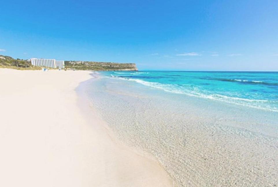 a white beach with the ocean in the background at Bonito apartamento con terrazas y aparcamiento. in Son Bou