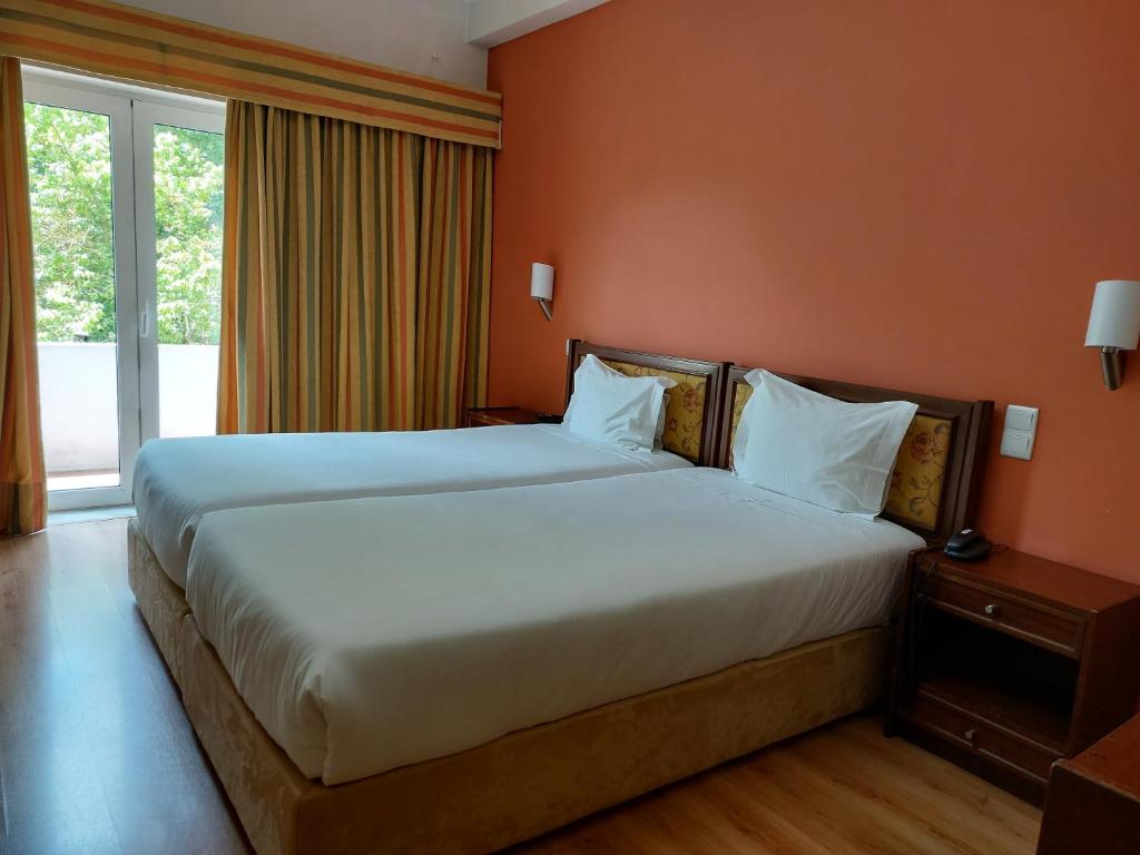 a hotel room with two beds and a window at Petrus Hotel in Chaves