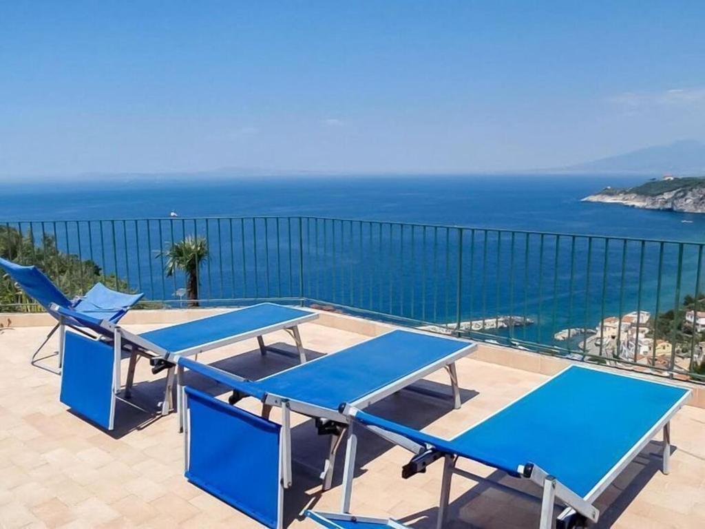 uma varanda com mesas e cadeiras azuis e o oceano em Villa Lobra em Massa Lubrense