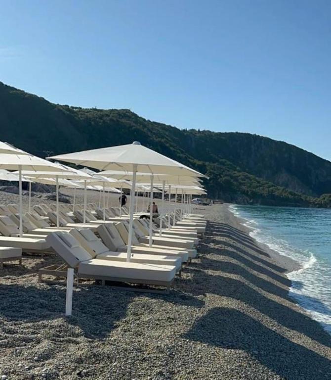 a row of white lounge chairs and umbrellas on a beach at Black Diamond Hotel Dhermi in Dhërmi