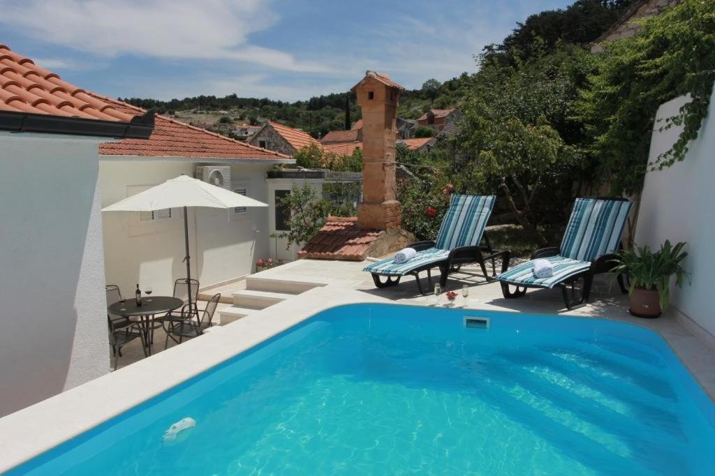 a pool with two chairs and a table and an umbrella at Holiday House Pine Tree in Nerežišća