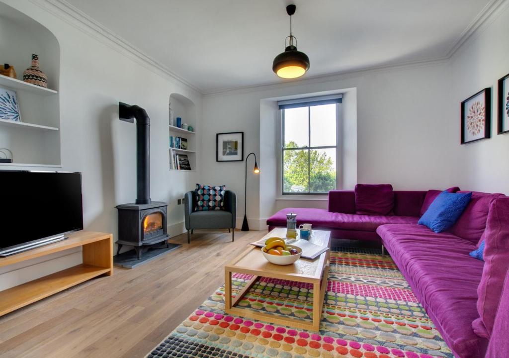een woonkamer met een paarse bank en een open haard bij Bath Cottage in Saundersfoot