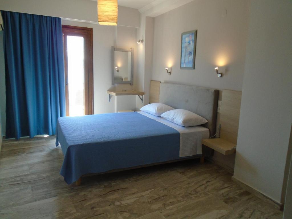 een slaapkamer met een bed met blauwe lakens en een raam bij Polyxeni Hotel in Pythagoreio