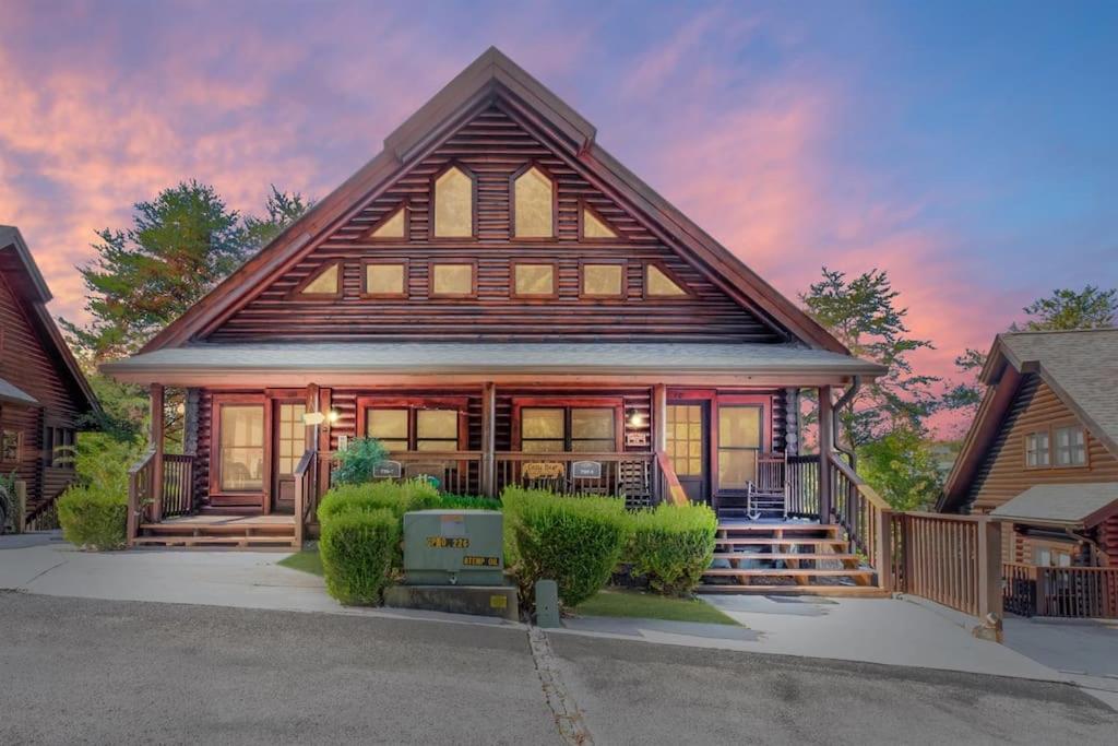 a house with a gambrel roof with a porch at 2 Miles from Dollywood Family Resort with Seasonal Outdoor Swimming Pool, Year around Heated Indoor Swimming Pool, Townhome Style Cabin, Private Hot Tub, Arcade, TV, Wifi, Kitchen with Refrigerator, Washer and Dryer in Pigeon Forge