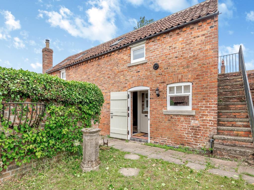 a brick house with a white door and a hedge at The Stables Cottage in Hemingby