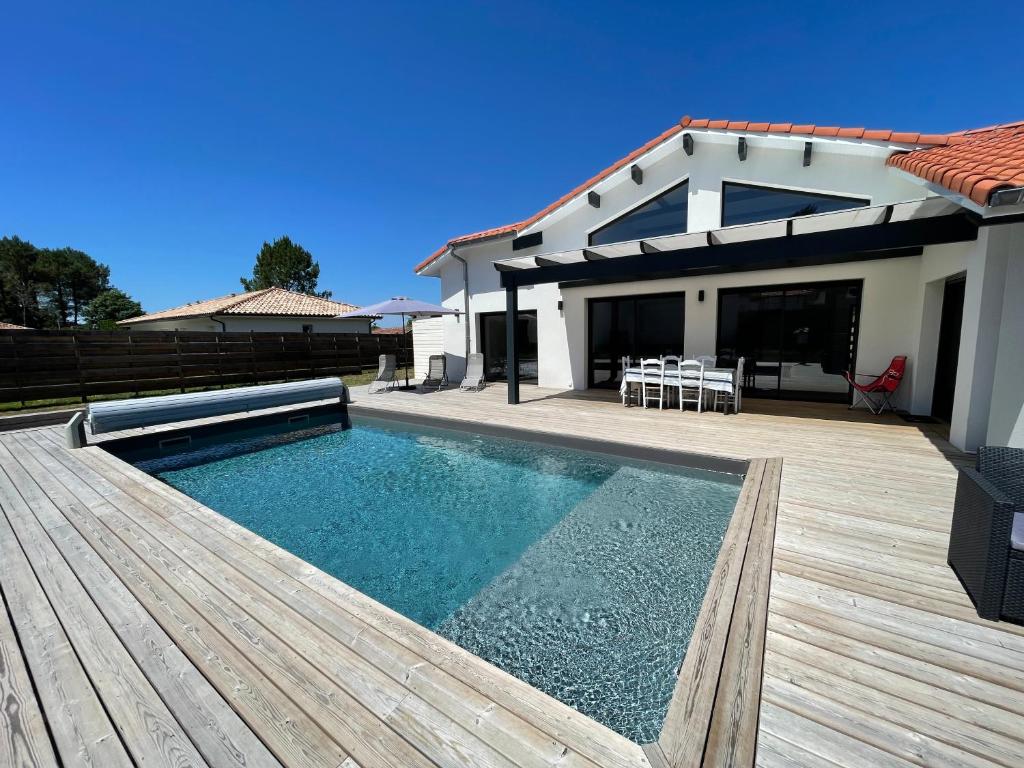 a house with a swimming pool and a wooden deck at Villa Pura Vida in Magescq