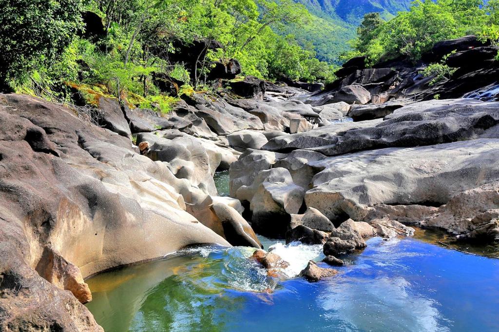 a river with rocks and blue water and trees at Chalé tribal in Alto Paraíso de Goiás