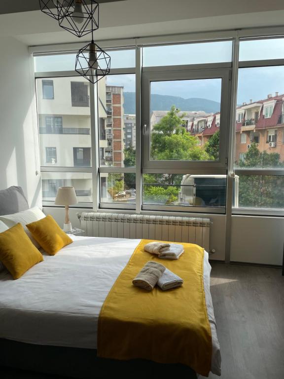 a bedroom with a bed with yellow sheets and windows at Kamche apartment in Skopje