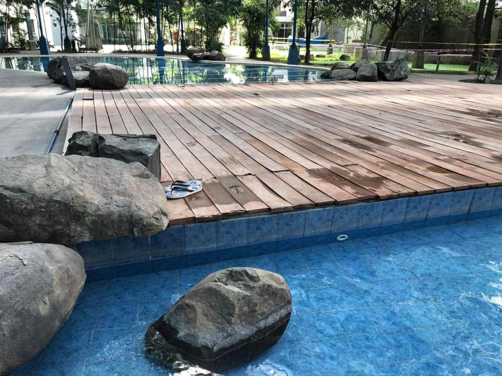 a swimming pool with rocks and a wooden deck at Kasara Urban Resort and Residences in Manila