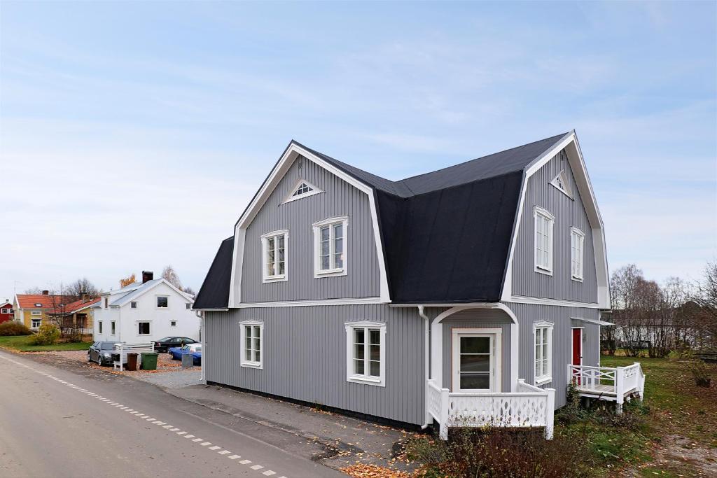 una casa gris con un techo negro al lado de una carretera en Guestly Homes - 4BR Charming Apartment, en Piteå