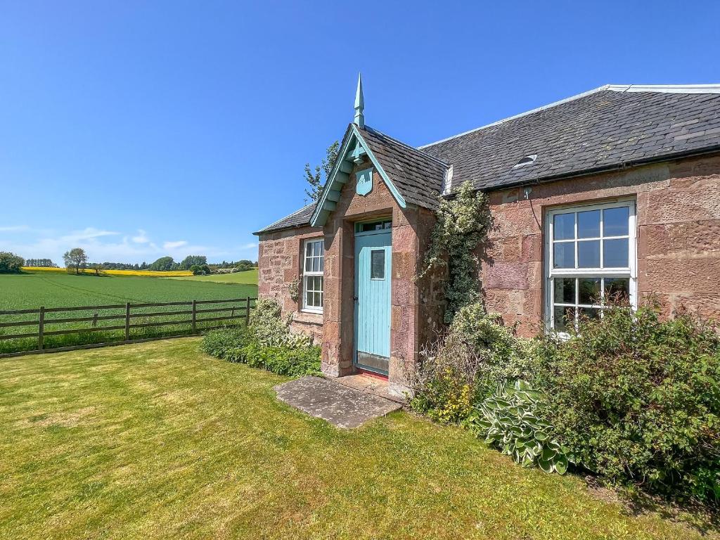 a brick house with a blue door in a field at Osprey Cottage - Uzq in Kirkton of Airlie