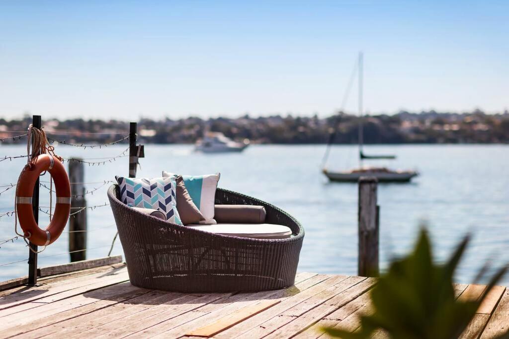 einen Korbstuhl, der auf einem Dock in der Nähe des Wassers sitzt in der Unterkunft Newly Reburbished Sydney Harbourfront Boathouse Escape in Sydney