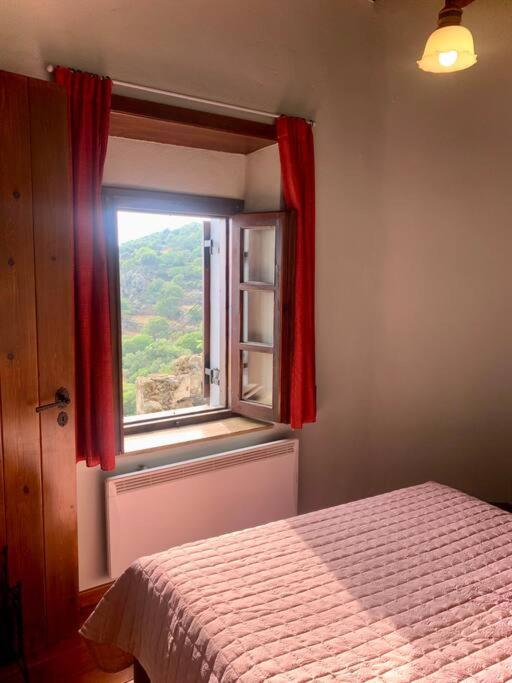 a bedroom with a bed and a window with red curtains at Cloud House on Nisyros in Emporeiós