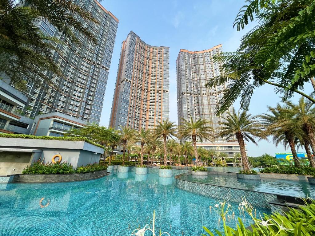 een groot zwembad met palmbomen en hoge gebouwen bij Gold Coast Sea View Apartments by Rentrooms in Jakarta