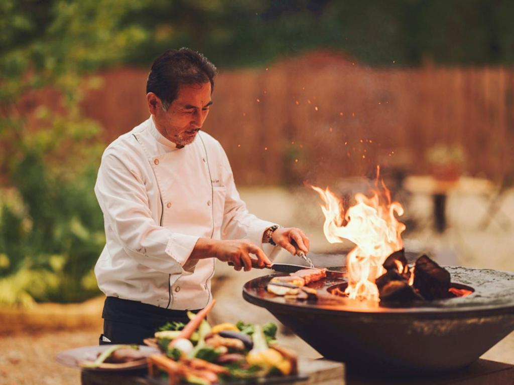 a man cooking food on a grill with fire at Premium villa glamping log cabin with stars and bonfire in Hokuto