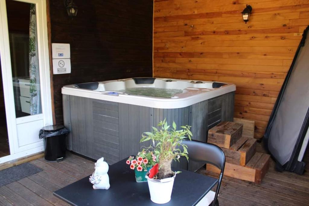 bañera de hidromasaje en un patio con mesa y mesa en Au coucher du soleil, chalet avec jacuzzi et sauna, en Vieux-CondÃ©