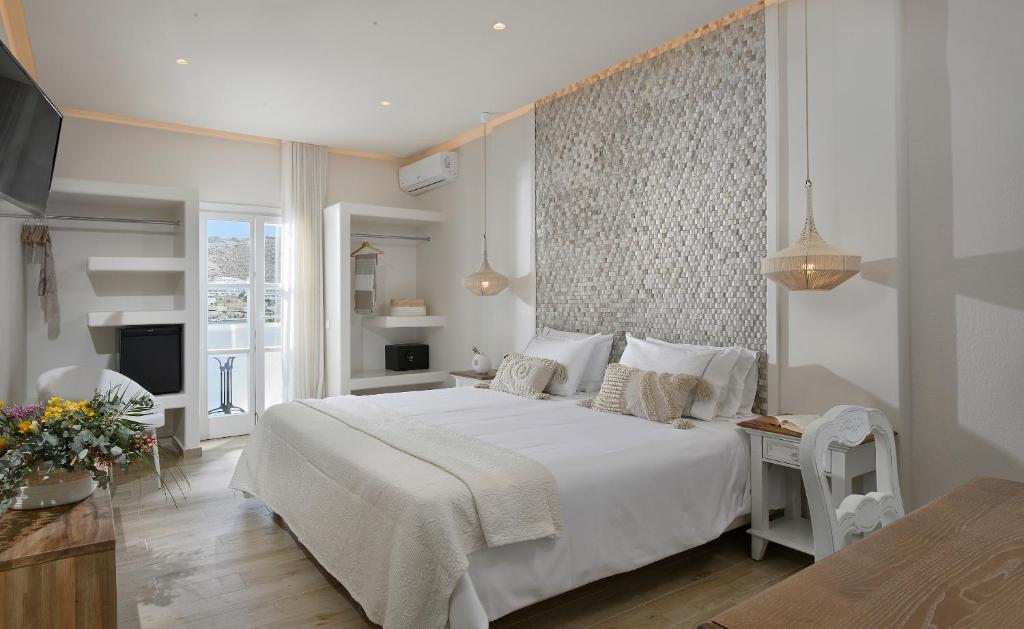 a white bedroom with a large bed and a tv at Erato Hotel Mykonos in Ornos