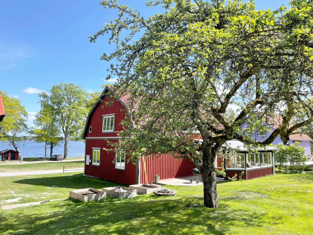 a red barn with a tree in front of it at Nice holiday home with a view of lake Asnen in Hulevik, Lonashult in Lönashult