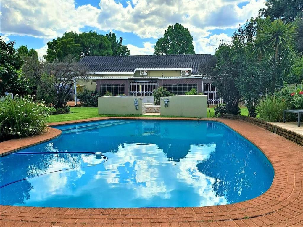 a blue swimming pool in front of a house at Rudys Guesthouse in Meyerton