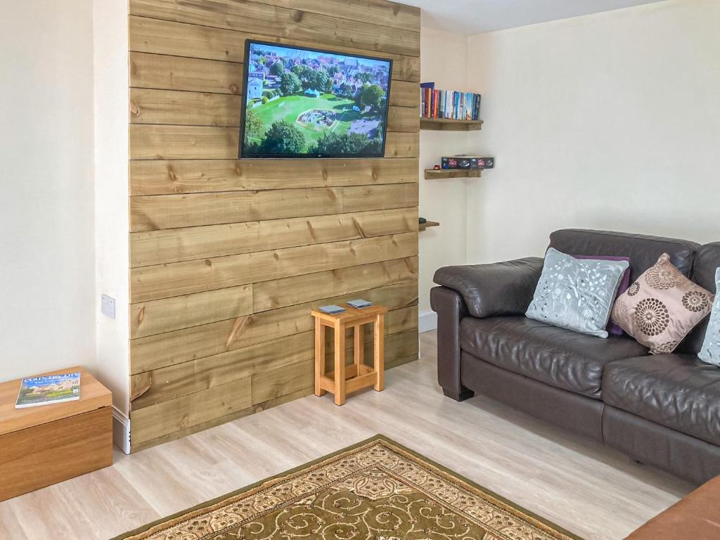 sala de estar con sofá y TV en la pared en The Grooms Cottage, en Mauchline
