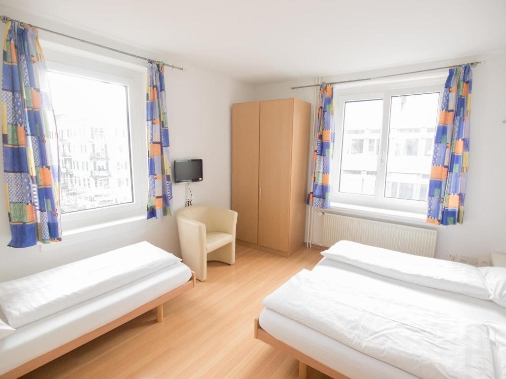 a bedroom with two beds and two windows at Hotel Gregory in Zürich