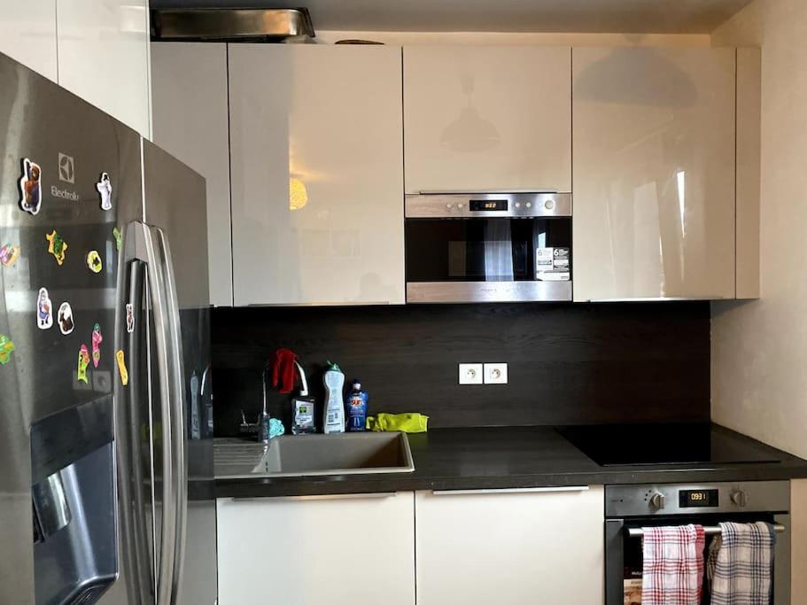 La cuisine est équipée de placards blancs et d'un réfrigérateur en acier inoxydable. dans l'établissement Appartement familial 3 chambres 15min PARIS metro, à Bois-Colombes