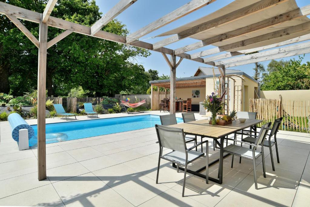 un patio avec une table et des chaises sous une pergola en bois dans l'établissement Maison Gwenan - Maison contemporaine pour 8 proche plage, à Saint-Cast-le-Guildo