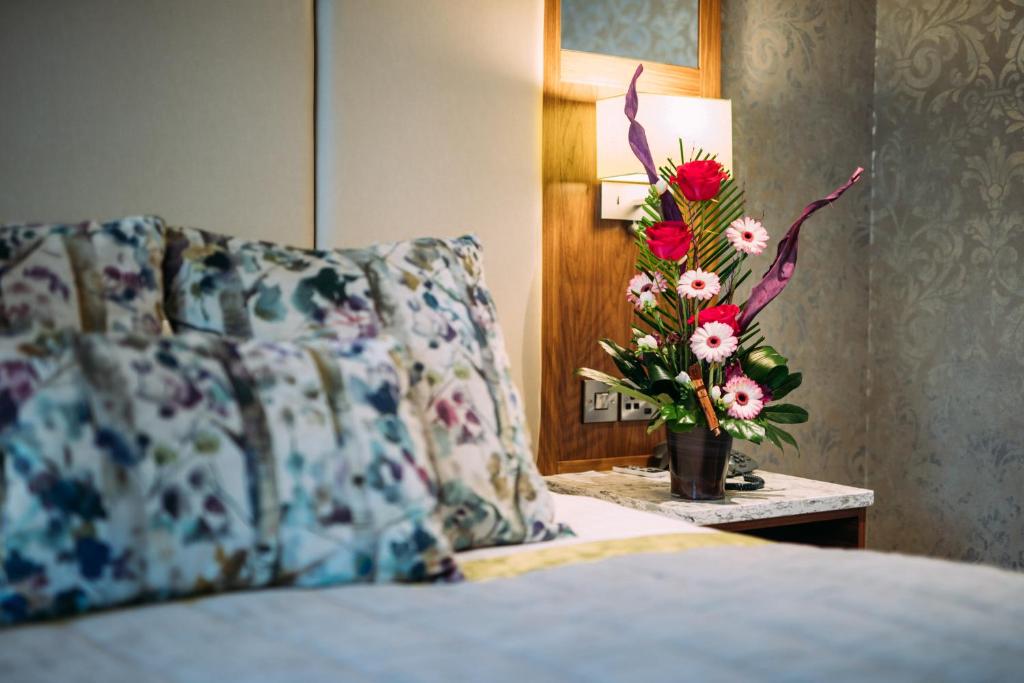 Una cama con una almohada y un jarrón de flores sobre una mesa en The Valley Hotel & Carriage Gardens, en Fivemiletown
