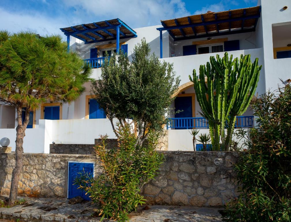 a white building with blue windows and trees at Meli Apartments near sea side in Kýthira