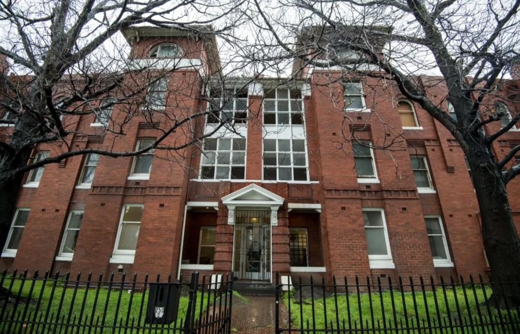 um edifício de tijolos vermelhos com uma cerca em frente em Fawkner Mansions Heritage Hotel em Melbourne