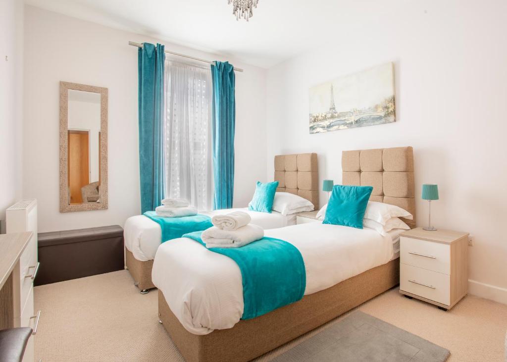 two beds in a bedroom with blue curtains at Castle Haven Apartment, Redhill in Redhill