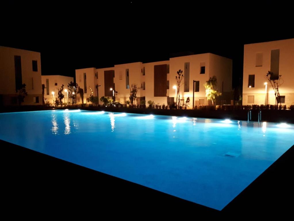 a large swimming pool in front of buildings at night at Bel Appartement Agadir Tamourit in Agadir