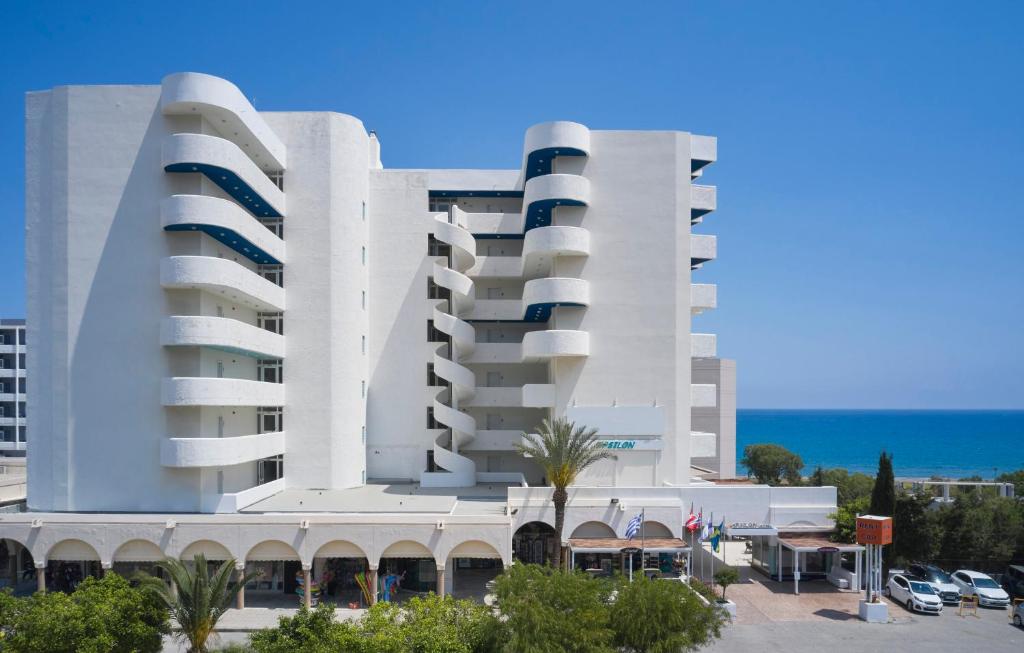 duży biały budynek z parkingiem i oceanem w obiekcie Epsilon Hotel Apartments w mieście Faliraki