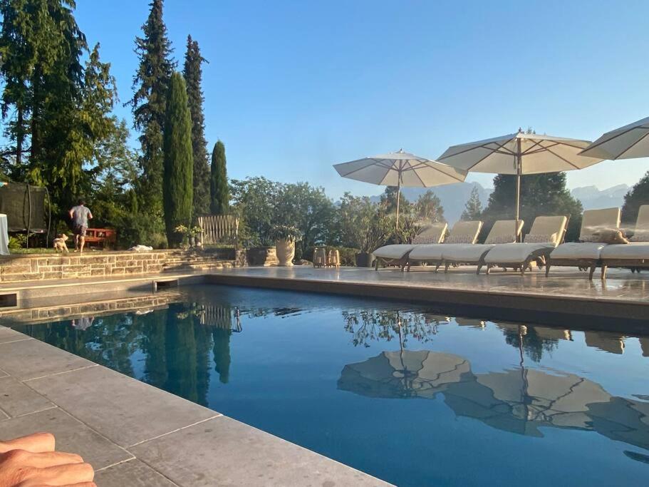 una piscina con sillas y sombrillas en Stunning Villa overlooking lake, en Le Châtelard-Montreux