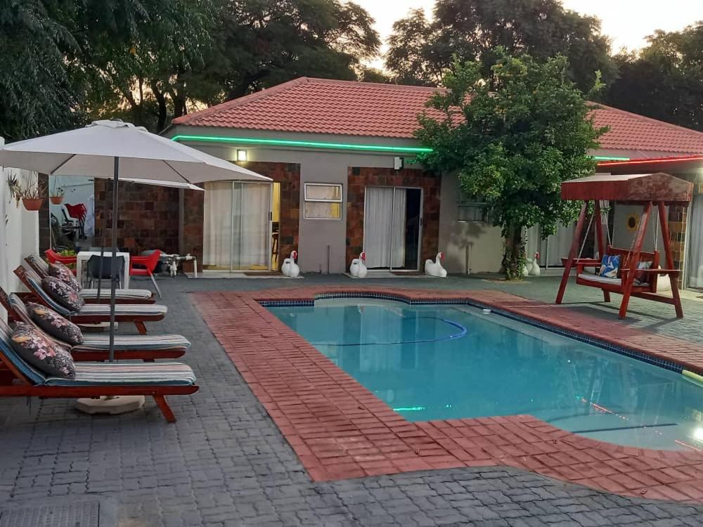 a swimming pool with two lounge chairs and an umbrella at Eagles Nest Self-Catering Apartments in Gaborone