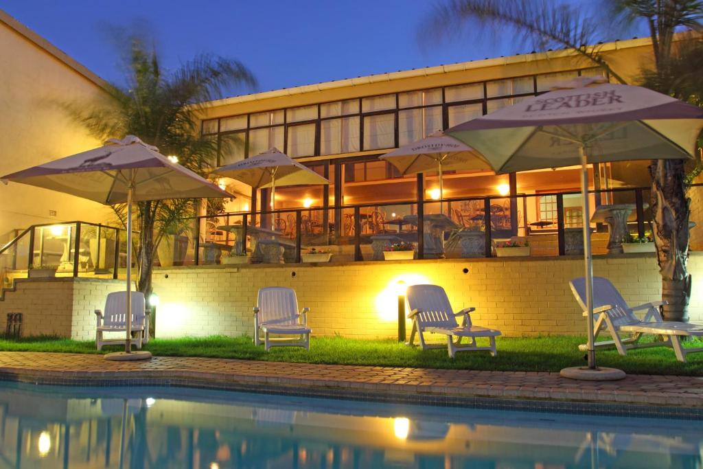 Un grupo de sillas y sombrillas junto a una piscina. en Hotel Portao Diaz, en Mossel Bay