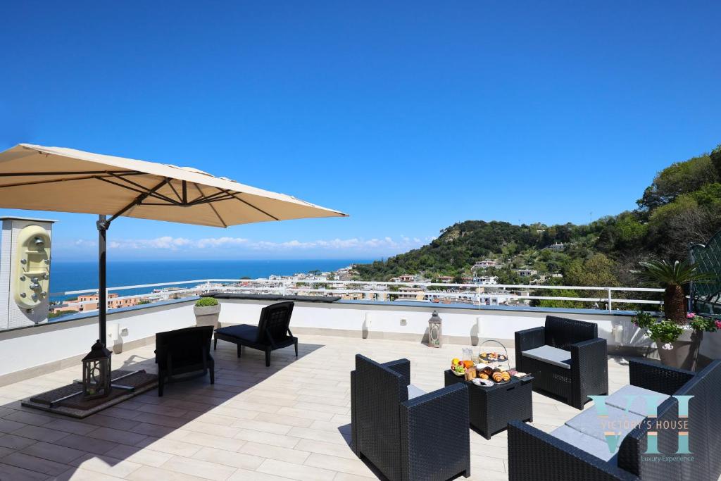 a patio with chairs and an umbrella and the ocean at Victory's Luxury House with Jacuzzi on the Roof in Ischia