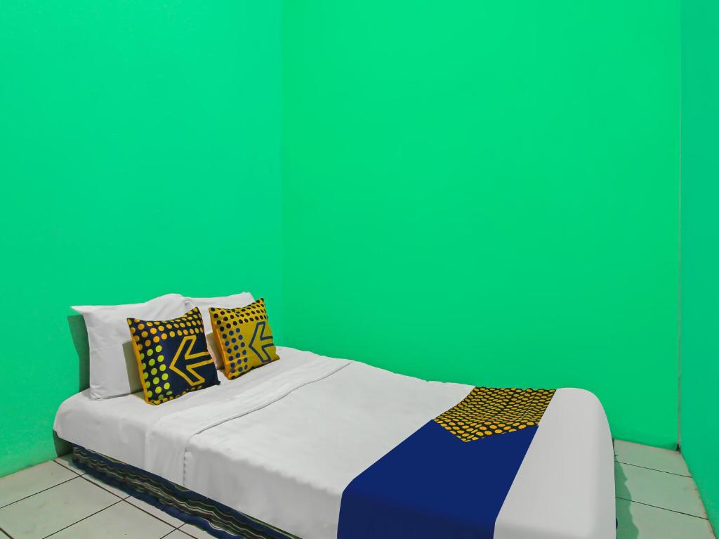 - un lit blanc avec des oreillers colorés contre un mur vert dans l'établissement SPOT ON 92610 Barokah Kostel Syariah, à Semarang
