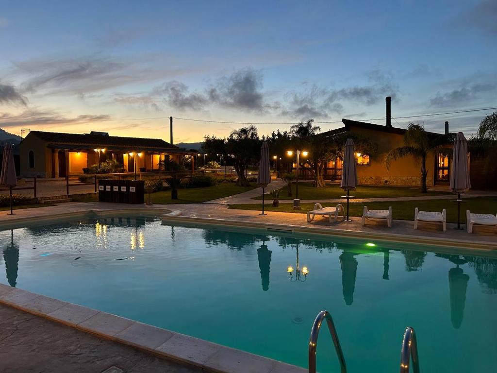 a swimming pool at dusk with a house in the background at Agriturismo l'Olivo in Calatafimi