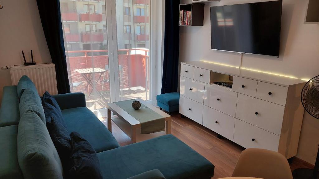 ein Wohnzimmer mit einem blauen Sofa und einem TV in der Unterkunft Apartament przy Łąkach - Zakodomki (Kraków) in Krakau