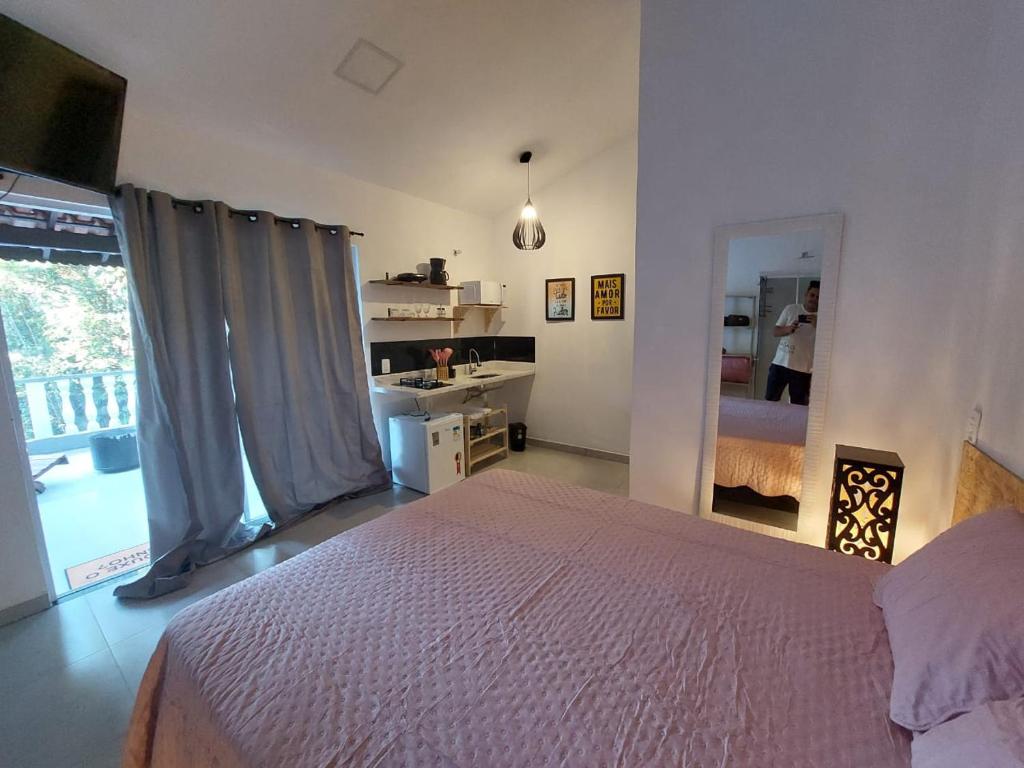 a bedroom with a bed and a kitchen with a window at Recanto da Floresta Suítes in Petrópolis