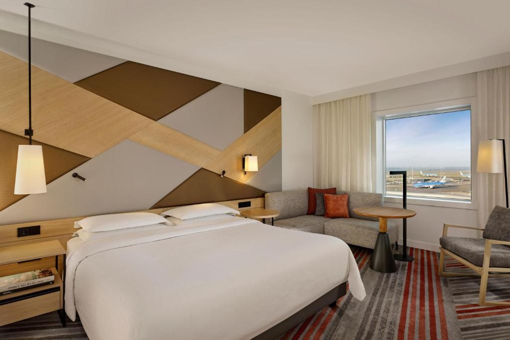 スキポールにあるSheraton Amsterdam Airport Hotel and Conference Centerのベッド、デスク、椅子が備わるホテルルームです。