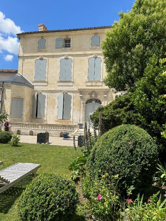un grand bâtiment avec des fenêtres et des buissons dans une cour dans l'établissement Le Jardin des Anges, à Saint-Jean-dʼAngély